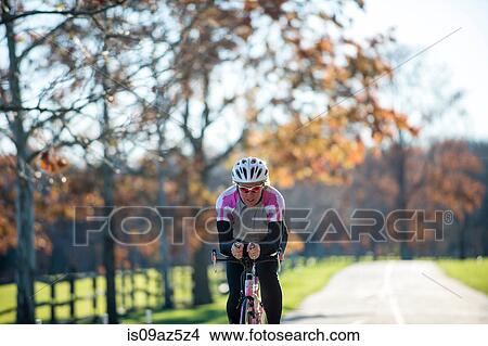 Cyclists cycling on tree lined road View Large Photo Image Picture - Cyclists cycling on tree lined road. Fotosearch