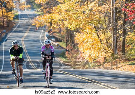 Cyclists cycling side by side on tree lined road View Large Photo Image Stock Image - Cyclists cycling side by side on tree lined road. Fotosearch