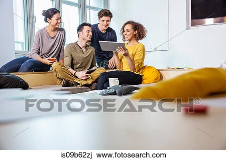 Stock Image - Digital designers on office sofa looking at digital tablet. Fotosearch