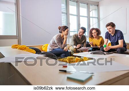 Stock Image - Digital designers on office sofa looking at digital tablet. Fotosearch