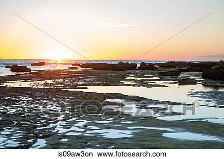 Picture - Distant view of woman at sunset on rocky beach, Cape of Trafalgar, Spain. Fotosearch