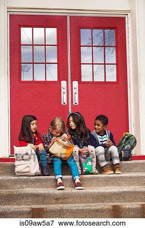 Stock Photo - Elementary schoolgirls and boys sitting on elementary school doorway stairs looking in satchel. Fotosearch