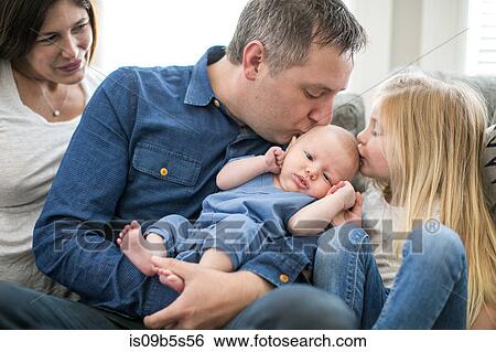 Stock Photograph - Family sitting on sofa, father and young girl kissing baby boy. Fotosearch