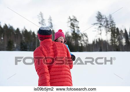 Stock Image - Father carrying young son in snow covered landscape. Fotosearch
