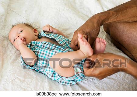 Stock Image - Father dressing up baby in bed. Fotosearch