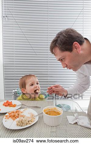 Father feeding son at dining table View Large Photo Image Picture - Father feeding son at dining table. Fotosearch