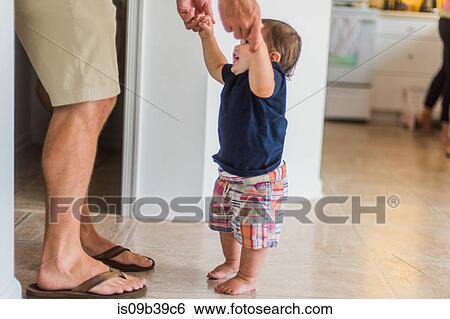 Stock Photograph - Father holding hands of toddler, guiding him to walk. Fotosearch