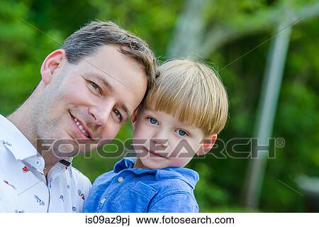 Father holding son looking at camera smiling View Large Photo Image Stock Image - Father holding son looking at camera smiling. Fotosearch