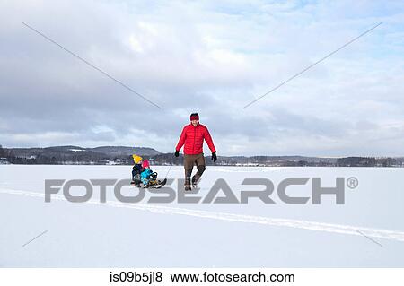 Father pulling sons along on sledge in snow covered landscape View Large Photo Image Stock Photo - Father pulling sons along on sledge in snow covered landscape. Fotosearch