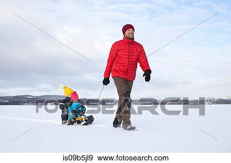 Father pulling sons along on sledge in snow covered landscape View Large Photo Image Stock Photo - Father pulling sons along on sledge in snow covered landscape. Fotosearch
