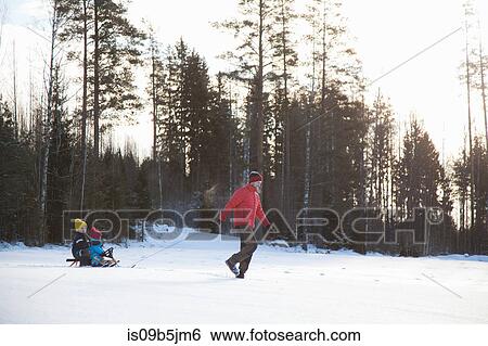 Stock Photograph - Father pulling sons along on sledge in snow covered landscape. Fotosearch