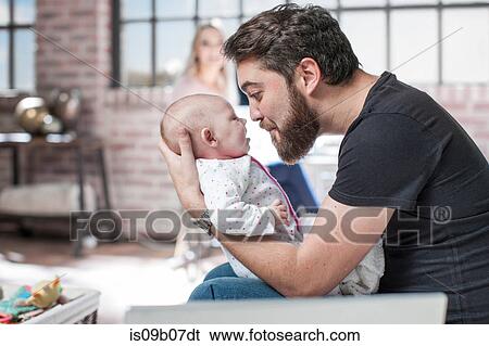 Father sitting, playing with baby daughter, mother sitting at desk, working, behind View Large Photo Image Stock Photograph - Father sitting, playing with baby daughter, mother sitting at desk, working, behind. Fotosearch