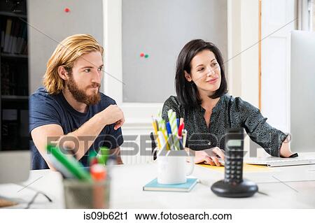 Stock Image - Female and male designers looking at computer in creative studio. Fotosearch