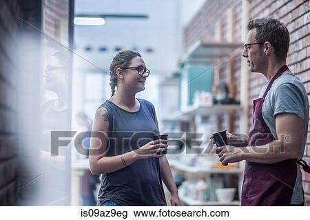 Stock Image - Female and male potter chatting over coffee in workshop. Fotosearch