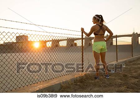 Female athlete daydreaming by wire fence at sunset, Van Nuys, California, USA View Large Photo Image Stock Photo - Female athlete daydreaming by wire fence at sunset, Van Nuys, California, USA. Fotosearch