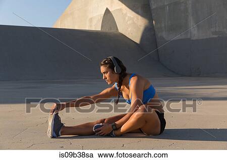 Stock Image - Female athlete with headphones, stretching, Van Nuys, California, USA. Fotosearch