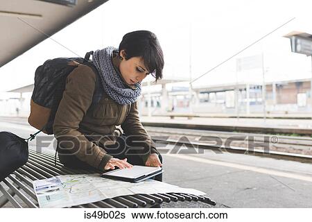 Stock Photograph - Female backpacker looking at map and digital tablet on railway platform. Fotosearch