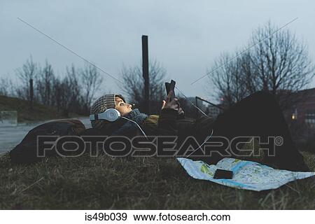 Female backpacker lying in city park at night looking at smartphone View Large Photo Image Stock Photo - Female backpacker lying in city park at night looking at smartphone. Fotosearch