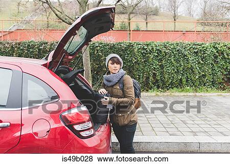 Stock Photo - Female backpacker removing sleeping bag from car boot in city. Fotosearch