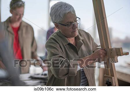Stock Image - Female carpenter putting up easel in furniture making workshop. Fotosearch