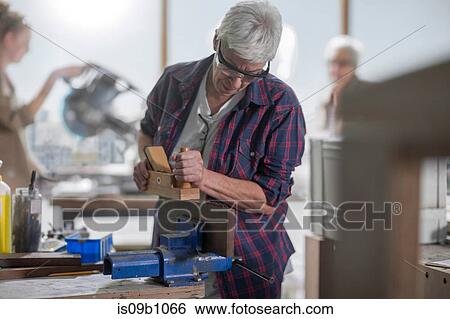 Stock Photograph - Female carpenter using wood plane in furniture making workshop. Fotosearch