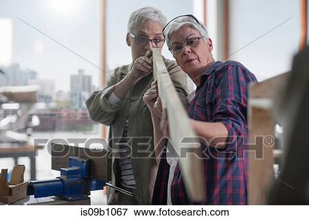 Stock Photo - Female carpenters inspecting wood plank in furniture making workshop. Fotosearch
