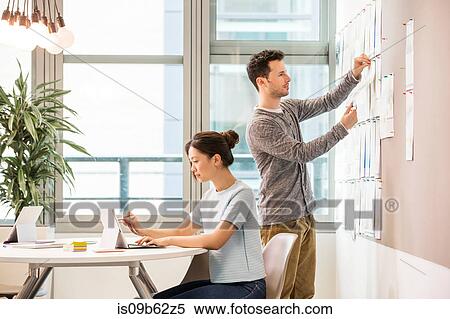 Female digital designer typing on laptop and colleague arranging mood board in office View Large Photo Image Stock Photography - Female digital designer typing on laptop and colleague arranging mood board in office. Fotosearch