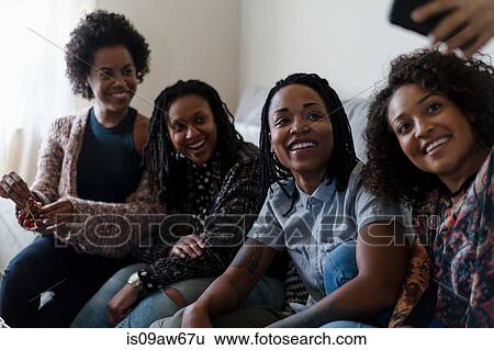 Female friends relaxing at home, taking self portrait using smartphone View Large Photo Image Stock Photograph - Female friends relaxing at home, taking self portrait using smartphone. Fotosearch