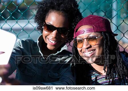 Stock Image - Female friends taking self portrait using smartphone. Fotosearch
