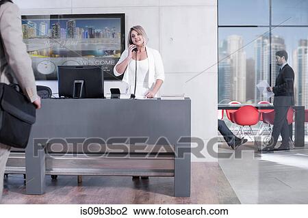 Stock Image - Female hotel receptionist talking on landline in hotel reception. Fotosearch