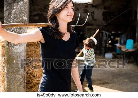 Stock Photo - Female organic farmer with pitch fork over her shoulder on dairy farm. Fotosearch