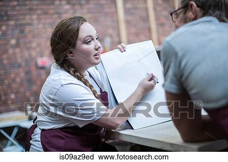 Stock Image - Female potter explaining ideas to trainee in workshop. Fotosearch