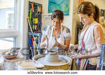 Stock Photograph - Female potter explaining to mature student making pot on potters wheel. Fotosearch
