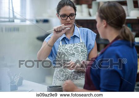 Female potter explaining tool to trainee in workshop View Large Photo Image Stock Photo - Female potter explaining tool to trainee in workshop. Fotosearch