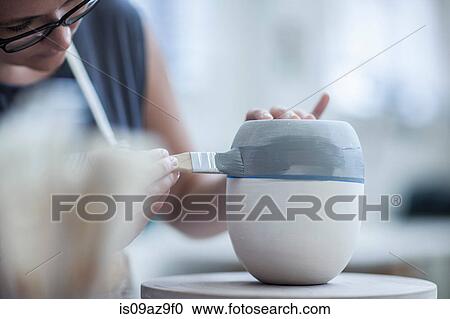 Stock Image - Female potter painting ceramic glaze on vase in workshop. Fotosearch