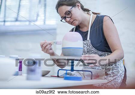 Stock Image - Female potter painting ceramic glaze on vase in workshop. Fotosearch