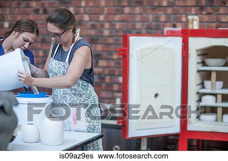 Stock Photograph - Female potter pouring ceramic glaze into bucket in workshop. Fotosearch