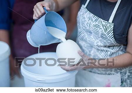 Stock Photograph - Female potter pouring ceramic glaze into vase in workshop. Fotosearch