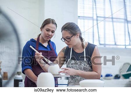 Female potter showing trainee how to glaze in workshop View Large Photo Image Stock Photo - Female potter showing trainee how to glaze in workshop. Fotosearch