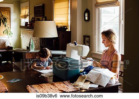 Female toddler colouring at table whilst mother sewing View Large Photo Image Stock Photograph - Female toddler colouring at table whilst mother sewing. Fotosearch