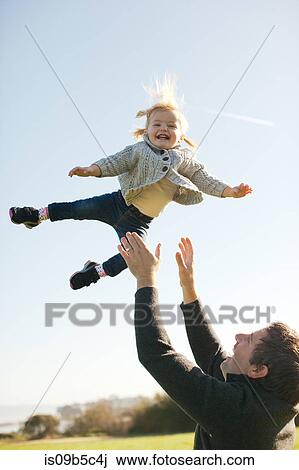 Stock Image - Female toddler thrown mid air by father against blue sky. Fotosearch