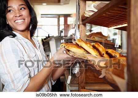 Stock Image - Female worker in bakery, putting fresh pasties into display cabinet. Fotosearch