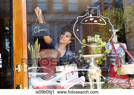 Stock Image - Female worker in bakery, turning sign to open. Fotosearch