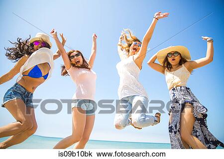 Stock Image - Four adult female friends jumping mid air on beach, Malibu, California, USA. Fotosearch