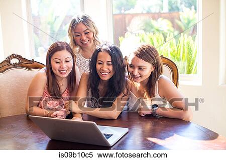 Stock Photography - Four adult female friends reading laptop at dining table. Fotosearch