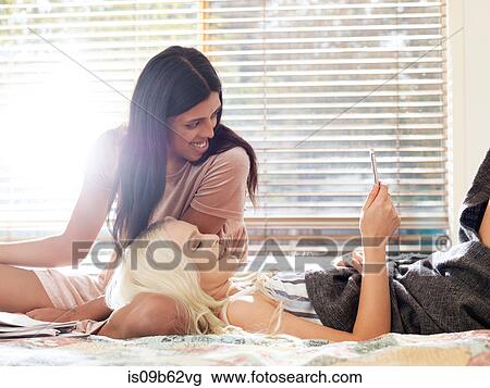Friends on bed looking at smartphone smiling View Large Photo Image Stock Image - Friends on bed looking at smartphone smiling. Fotosearch