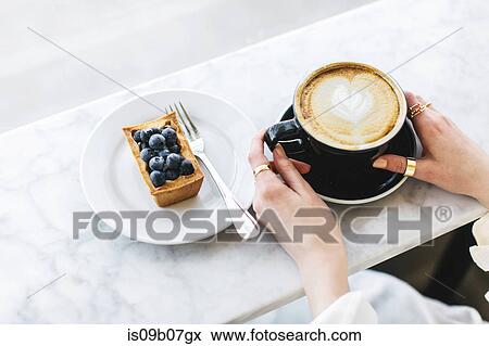 Fruit tart and woman's hands holding frothy coffee View Large Photo Image Stock Photo - Fruit tart and woman's hands holding frothy coffee. Fotosearch