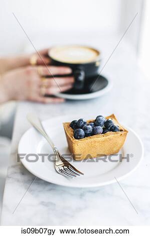 Fruit tart and woman's hands holding frothy coffee View Large Photo Image Stock Photo - Fruit tart and woman's hands holding frothy coffee. Fotosearch