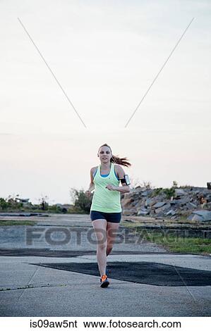 Stock Photograph - Full length front view of woman wearing activity tracker jogging. Fotosearch