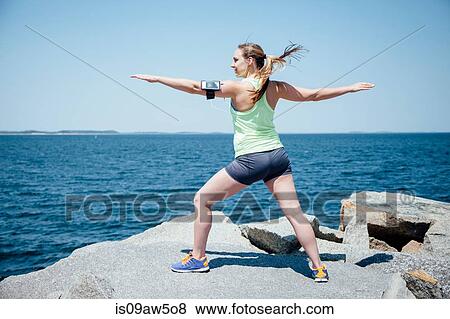 Full length rear view of woman wearing activity tracker on rocks by ocean, arms open exercising View Large Photo Image Stock Photo - Full length rear view of woman wearing activity tracker on rocks by ocean, arms open exercising. Fotosearch